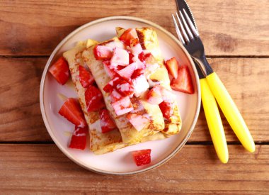 Crepe rolls with cottage cheese and raisin filling with condensed milk and strawberry topping