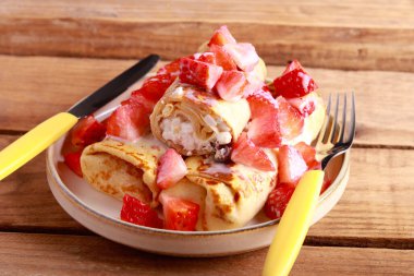 Crepe rolls with cottage cheese and raisin filling with condensed milk and strawberry topping
