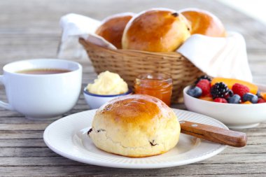 Kuru üzümlü çörek, tereyağı, marmelat ve böğürtlen ile servis edilir.