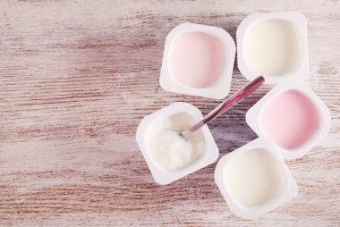 Plastik bardaklarda, ahşap masada çeşitli yoğurtlar.