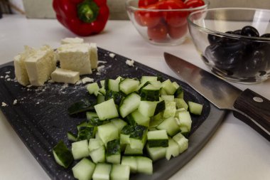 Sebze yemeği hazırlama süreci. Yunan Salatası Malzemeleri. Ön planda dilimlenmiş peynir ve salatalık. Sağlıklı ev yemeği konsepti.