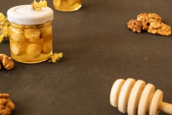 A jar of honey with hazelnuts on a dark table. In the background are peeled walnuts and in the foreground a honey spoon. Healthy food for strong immunity