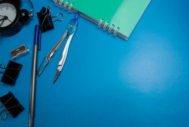 Mavi arka planda çeşitli kırtasiye malzemeleri. Not defteri, klasörler, pusulalar, açacağı, kalem ve daha fazlası. Okul için hazırlanılıyor.