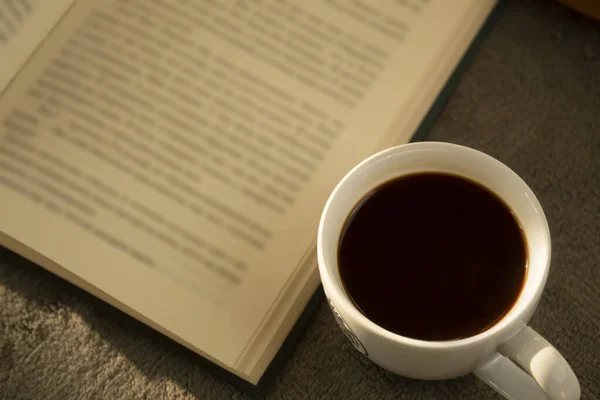 A cup of hot coffee and a book on a gray plaid. Warm homely atmosphere. View from above.