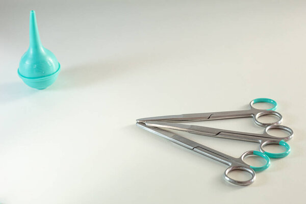 Surgical scissors and a syringe (enema bulb) lie on a white table. Medical background with free space. Photo in minimalism style.