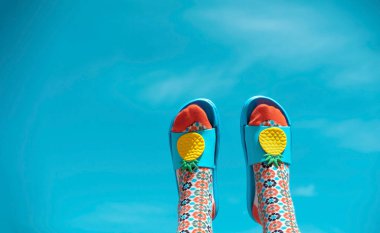 Renkli desenli çorapları ve mavi parmak arası terlikleri olan genç bir kadın. Yaz konsepti