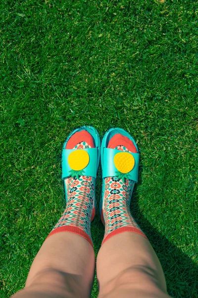 Feet of a young woman with colorful socks and blue flip-flops on grass. Summer concept.