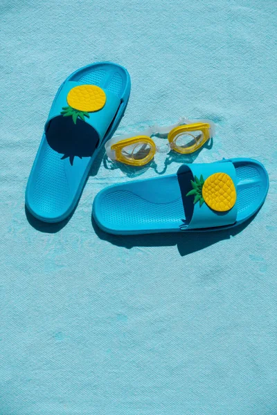 Blue pool sandals and yellow pool goggles on a blue beach towel. Summer concept. Vertical picture.