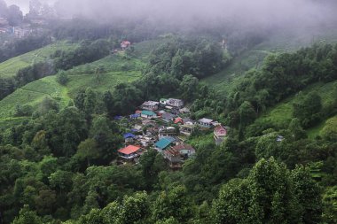 Puslu ve bulutlu dağ köyünün panoramik manzarası muson mevsiminde yeşil ormanlarla çevrili, Hindistan 'ın batısındaki Darjeeling Hill istasyonu yakınlarında.