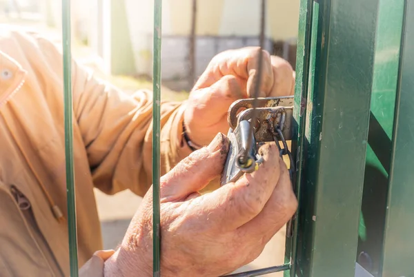 Hands of an older man dirty from work opening a padlock