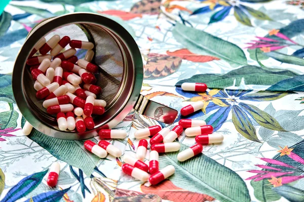 Bottle full of red and white pills on top of a table with a tropical pattern.