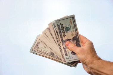 Man's hand holding a pile of dollars, on a white background.