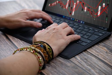 Organized and Focused: Woman Typing on Computer and Monitoring Graphs on a Wooden Table