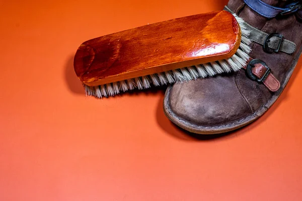Vintage shoe care tools: worn shoe, leather strips and wooden brush on brown background