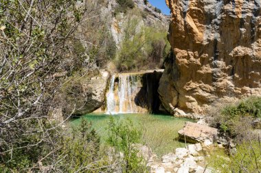 İspanya, Alquezar 'da bir yaz günü, arka planda açık mavi su ve dağlarla birlikte Vero nehri kanyonunda huzurlu bir şelale.