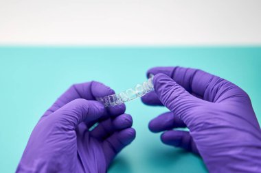 Diş teknisyeni, diş laboratuvarında görünmez bir desteğe sahip, mor eldivenler ve yeşil bir masa giyiyor..