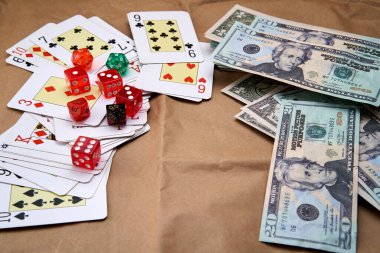 Poker kartları, farklı renkte zarlar ve dolarlar karton gibi bir yüzey üzerinde yatıyor..