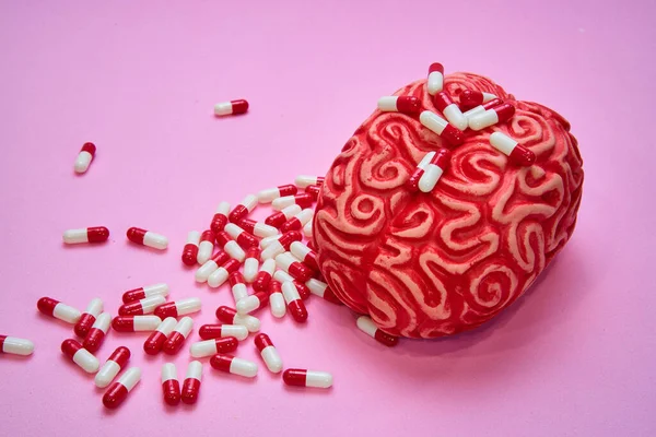 Kırmızı insan beyni, pembe bir masa üzerinde kırmızı ve beyaz haplar ve kapsüllerle dolu..