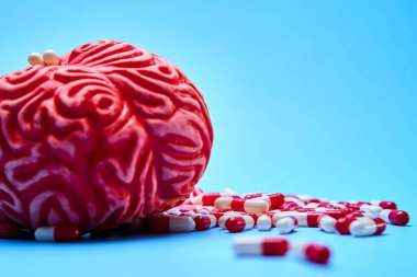 Kırmızı ve beyaz haplarla dolu kırmızı beyin, mavi bir yüzey üzerinde. Bağımlılık kavramı.