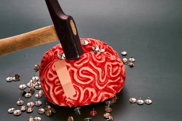 Hammer hits red human brain filled with thumbtacks on dark background. Cognitive repair.
