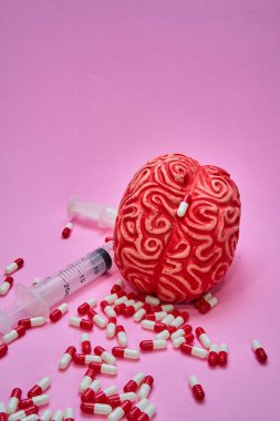 İki şırıngalı kırmızı insan beyni ve pembe bir masanın üzerinde kırmızı ve beyaz haplar ve kapsüller..