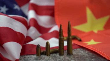 Amerikan ve Çin bayrağının ortasında tanınmayan birinin eli farklı boyutlarda bir avuç mermiyi topluyor.