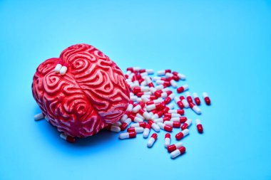 Kırmızı ve beyaz haplarla dolu kırmızı beyin, mavi bir yüzey üzerinde. Bağımlılık kavramı.