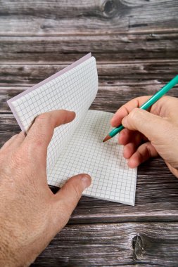 Tahta masadaki yeşil kalemle not defterine yazı yazan ellerin üst görüntüsü. 