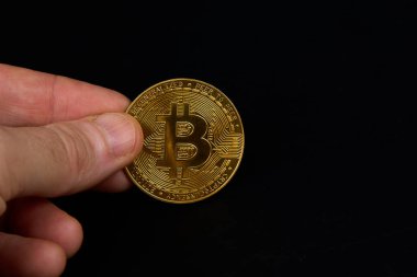 Görüntüde, birisi parlayan altın bir bitcoin 'i parmaklarıyla tutuyor. Arkaplan tahtadan yapılmış gibi görünüyor ve bitcoin metalik bir parıltıya sahip.
