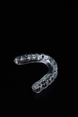 Koyu siyah bir yüzey üzerinde şeffaf bir ağız koruyucusu görünür. Sembolizm ve natürmort fotoğrafçılıkla çarpıcı bir monokromatik görüntü oluşturur.