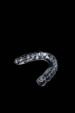 Pürüzsüz, siyah bir yüzeye uzanan temiz bir ağız koruyucudur. Görüntü bir simetri ve zarafet hissi tasvir ediyor, karanlığın ipuçları ve elektrik mavisi bir dokunuş.