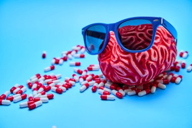 Mavi bir yüzey üzerinde haplarla güneş gözlüğü takan bir beynin akıl sağlığının temsili..