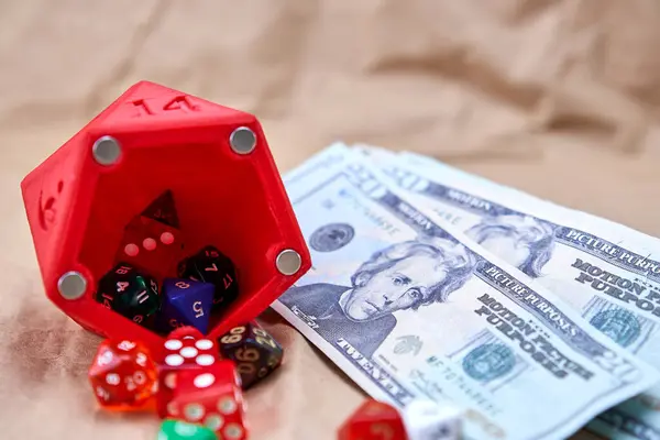 Çeşitli boyutlarda ve renklerde zarlar, zarlar şeklinde kırmızı bir zar ve birkaç dolar şeklinde, karton benzeri bir yüzey üzerinde.