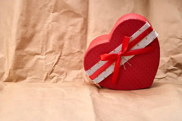 Kırmızı kalp şeklinde bir hediye, karton desenli bir arka planda.