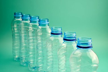 Bir sıra düzgün düzenlenmiş plastik şişeler canlı yeşil bir zemin üzerinde duruyor, geri dönüşüme hazır..