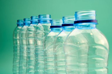 Bir sıra düzgün düzenlenmiş plastik şişeler canlı yeşil bir zemin üzerinde duruyor, geri dönüşüme hazır..