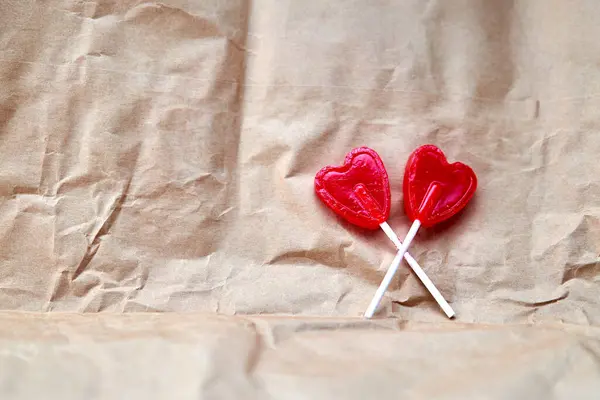 İki kırmızı kalp şeklinde lolipop karton bir arka planda yan yana..