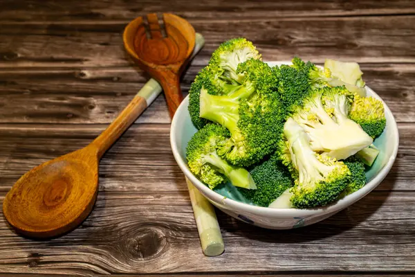 Tahta masaya saplı taze brokoli parçalarının üst görüntüsü. Gün ışığında mutfak kaşıklarıyla birlikte.