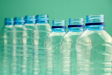 Yeşil arka planda sıralanan farklı şekil ve boyutlarda şeffaf plastik şişeleri yakın plan