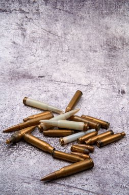 From above of collection of fired golden bullets and unfired cartridges with white plastic case arranged on rough floor at daytime clipart