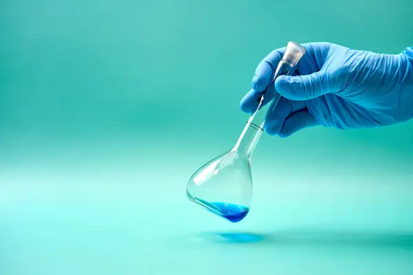 Laboratuvarda yapılan deney sırasında lateks eldivenli, elinde mavi kimyasal madde şişesi tutan tanınmayan bir araştırmacının eli.