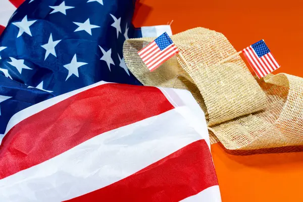 Büyük Amerikan bayrağı ve turuncu arka planda iki küçük bayrak.