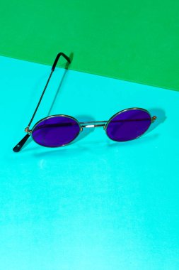 Mavi ve yeşil arka planda yuvarlak mor güneş gözlüğü.