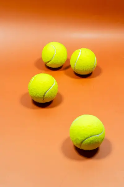 Turuncu bir yüzeyde parlak sarı tenis topları yığını.