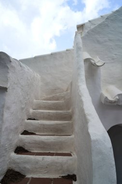 Binibeca, Menorca 'daki beyaz merdivenlerin büyüleyici manzarası, mavi gökyüzünün arka planına doğru gidiyor. Mimari eşsiz bir tasarım sergiliyor..