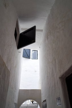 Binibeca, Menorca 'daki dar geçitte beyaz duvarlar, siyah panjurlar ve gökyüzüne bir bakış var..