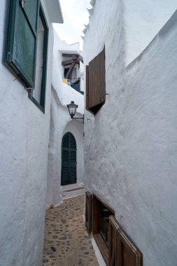 Binibeca, Menorca 'da dar bir sokak, beyaz yıkanmış binalarla dolu, pencereler ve kapılar ahşap panjurlarla kaplı..