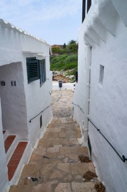 Binibeca, Menorca 'da manzaralı bir yürüyüş. Beyaz binalar ve aşağı doğru giden taş basamaklar var..