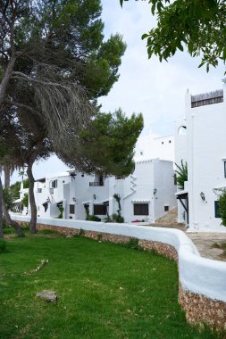Binibeca, Menorca: Beyazlatılmış binaların büyüleyici manzarası, yemyeşil çimenler ve eşsiz mimariyi gösteren taş bir duvar.