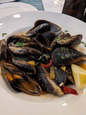 Lezzetli bir tabak midye, taze otlar, limon ve dolmalık biberle servis ediliyor. Bu deniz ürünleri yemeği restoranda eğlenmeye hazır..